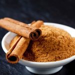 Bowl of cinnamon powder and two cinnamon sticks Superfood, Ceylon-Zimt, Zimt, Pulver, Stangen, Schalchen, schwarzer Untergrund, Schiefer